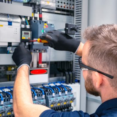 Man with gloves and safety glasses working on a panel board